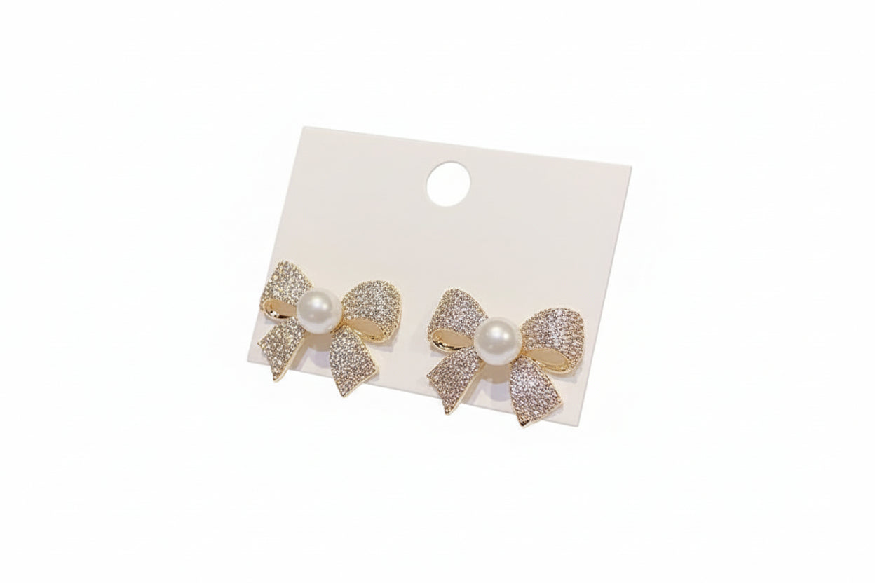 Bow-shaped earrings with pearls on a white card held by a hand.