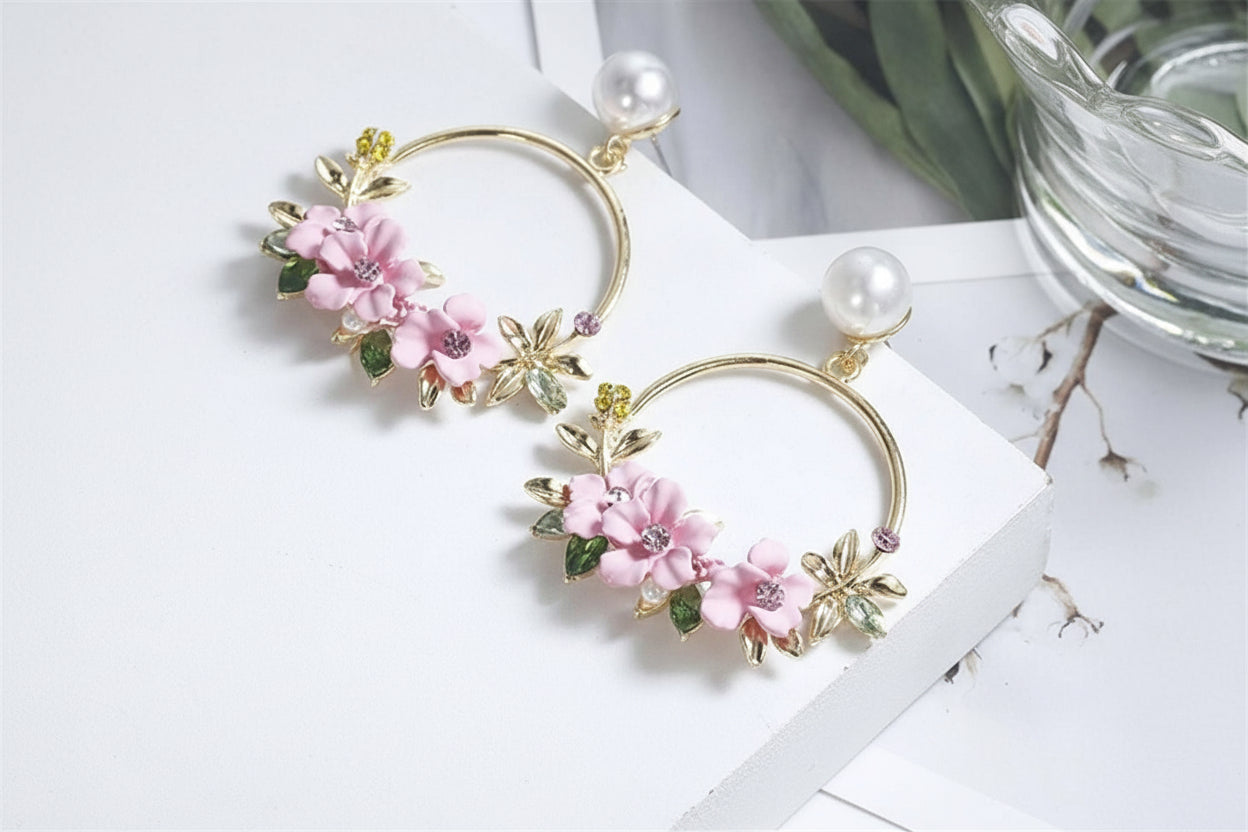 Floral hoop earrings with pink flowers and gold accents on a white surface.