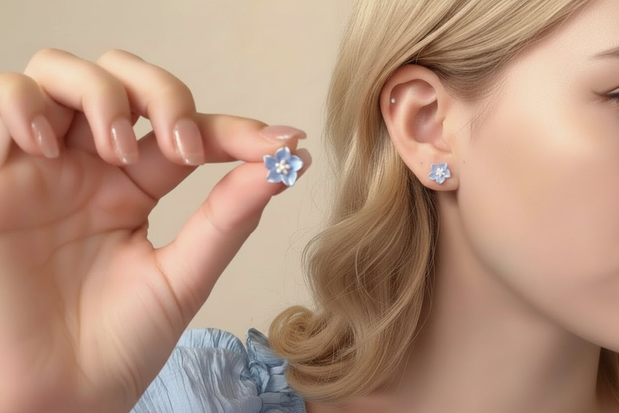 Woman wearing blue flower earrings with a hand holding one closer to the camera.